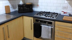 A kitchen with wooden cabinets, a gas stove, an oven, and a black countertop. - Fabulous, 2 bed apt, 10 mins from City Centre (Glasgow)