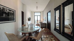 Habitación de hotel con mesa de vidrio, dos sillas, sofá, espejo grande y suelo estampado.