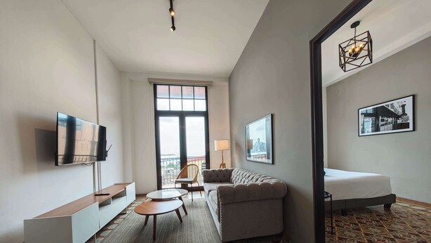 Habitación de hotel con sofá, una mesita, televisor montado en la pared, cama y suelo estampado, además de vistas por la ventana.