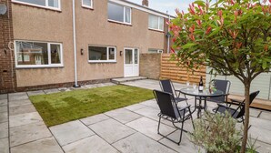 A residential backyard with a paved patio, a small lawn, and a dining table with chairs. - Willows (Corbridge)