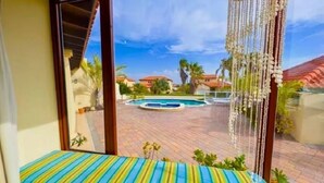 Un balcón con un cojín a rayas, una piscina y vista a una zona residencial.