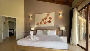 Cama bem arrumada com edredom branco e almofadas, cabeceira de madeira, duas luminárias de mesa e um quadro de estrelas vermelhas.