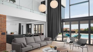 Un salon moderne avec un canapé gris, une table basse et un espace aménagé au bord de la piscine, comprenant des chaises longues.