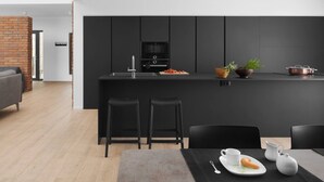 Une cuisine moderne dotée d’un îlot central, de tabourets de bar noirs et d’un coin repas avec une table dressée pour deux personnes.