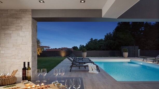 Un espace piscine extérieur moderne, aménagé avec un coin repas comprenant une table, des verres à vin, des collations et des chaises longues.
