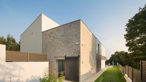 Une maison moderne avec une façade en pierre, un toit plat et une pelouse bien entretenue.