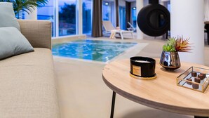 Uma área interna de piscina moderna, com um sofá, uma mesa com vela e uma planta decorativa.