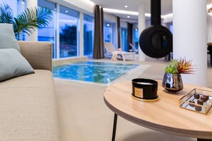 Un espace piscine intérieur moderne, aménagé avec un canapé, une table ornée d’une bougie et une plante décorative.
