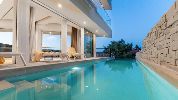 Uma área moderna à beira da piscina, com piscina transparente, espreguiçadeiras e uma parede de pedra.