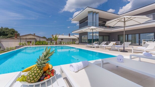A modern pool area with lounge chairs, a fruit bowl, and a two-story building with large windows. - Luxury Villa Nimai Luce Istria with Heated Pool (Kastelir)
