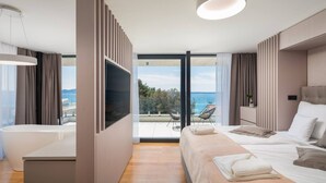 A modern hotel room with a large bed, a bathtub, a TV, and a balcony with a view of the sea. - Luxury Villa Idria Zadar with Heated Pool (Petrčane)