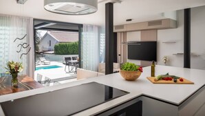 A modern kitchen with a large island, a built-in oven, and a view of a swimming pool. - Luxury Villa Idria Zadar with Heated Pool (Petrčane)