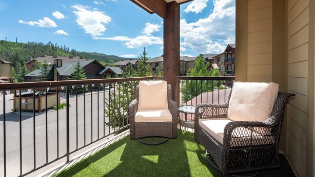 A balcony with wicker chairs and a small table, overlooking a residential area with houses and trees.