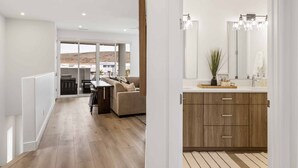 Una cocina moderna con armarios de madera y una isla grande, un área de comedor con sofá y mesa, y vista a un paisaje desértico a través de puertas correderas amplias.