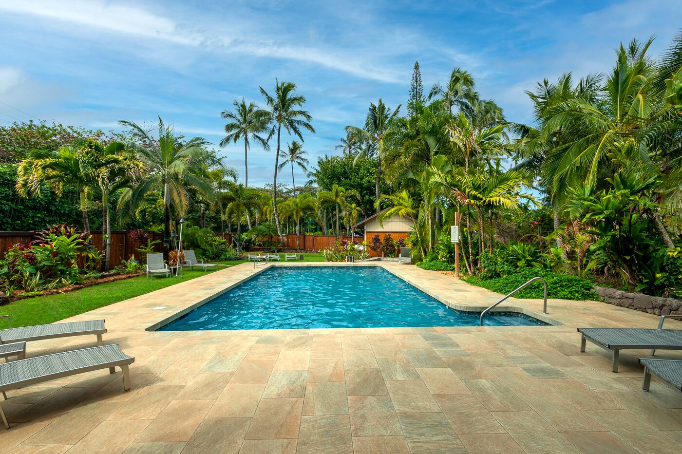 A rectangular swimming pool with a tiled deck, surrounded by palm trees and lush greenery.