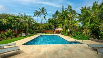 A rectangular swimming pool with a tiled deck, surrounded by palm trees and lush greenery.