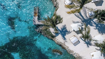 An aerial view of a beach with clear turquoise waters, a wooden pier, and white beach umbrellas.