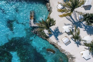 An aerial view of a beach with clear turquoise waters, a wooden pier, and white beach umbrellas. - Kwanza Resort By SUNRISE (Kizimkazi)