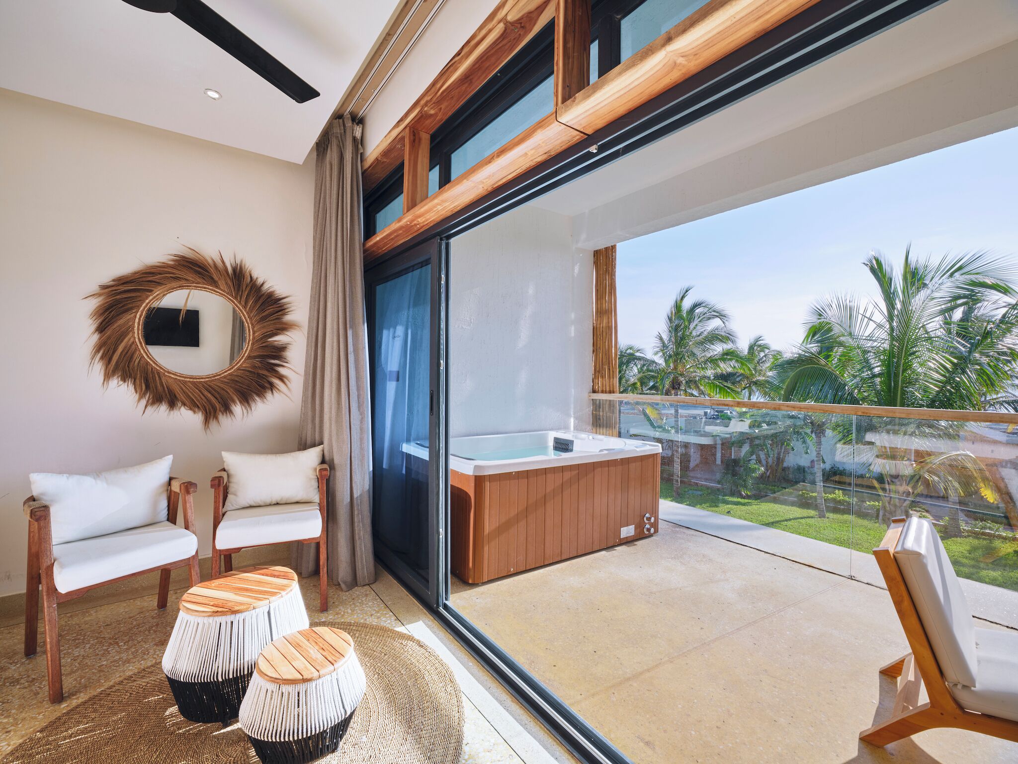 A modern bathroom with a large window, a wooden bathtub, and a round mirror.
