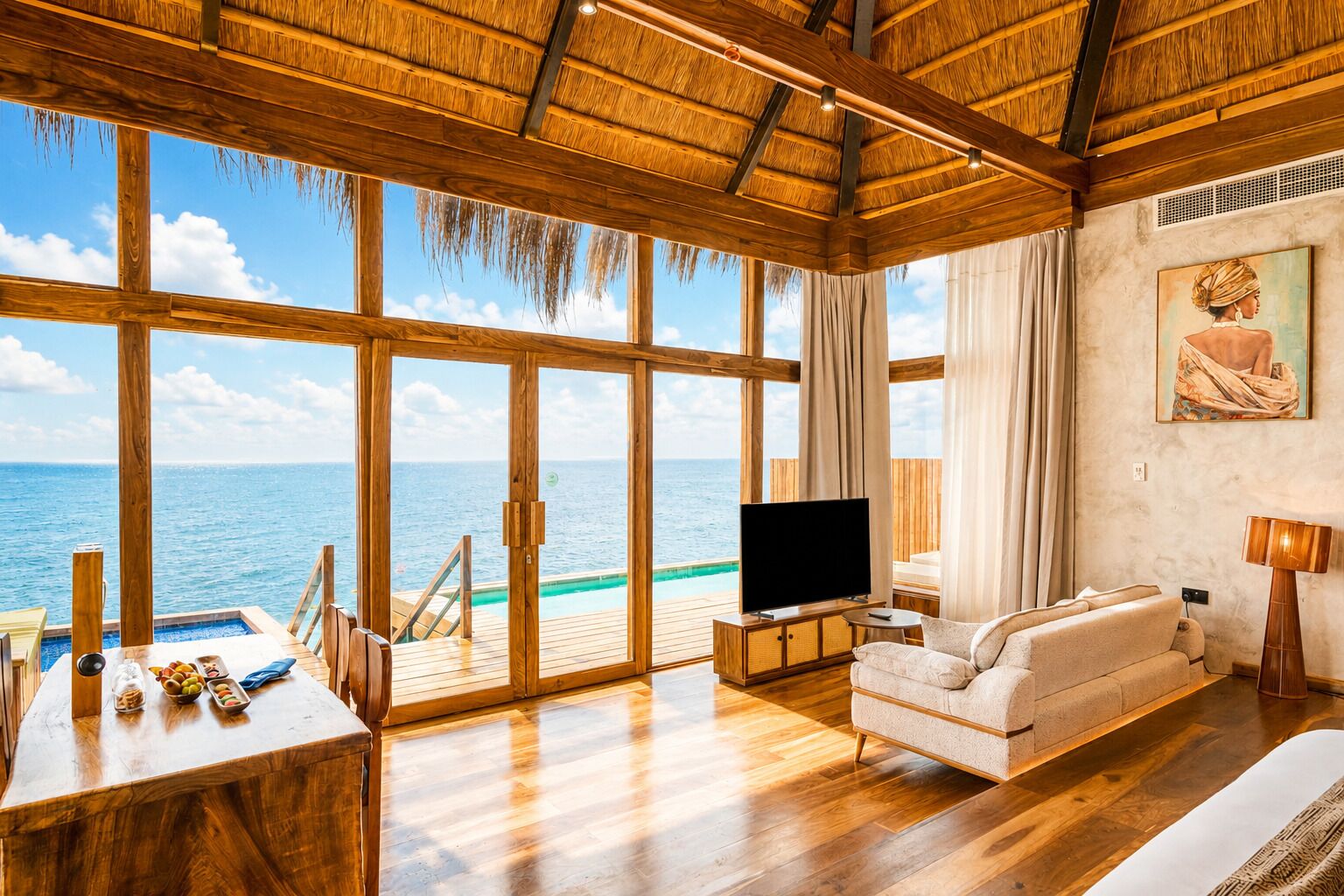 A spacious living area with a large TV, wooden flooring, a sofa, and a view of the ocean.