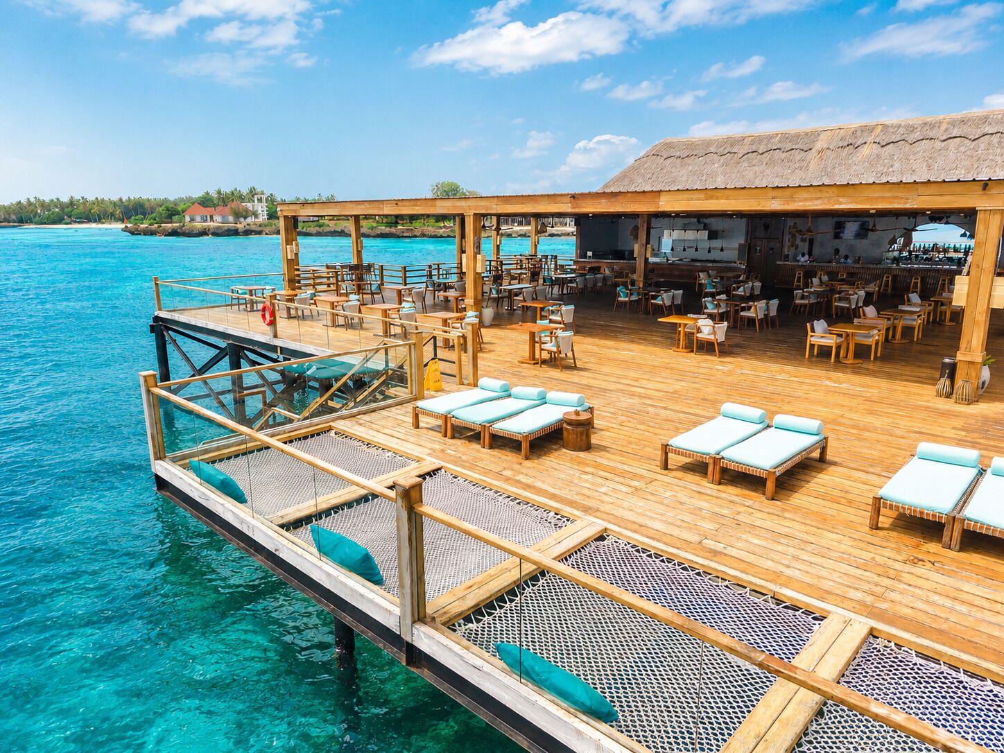 Terraza de madera con sillones y mesas, con vista a aguas turquesas.