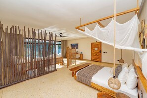 Un dormitorio amplio con una cama grande, un banco de madera, un dosel colgante sobre la cama y vistas al exterior.