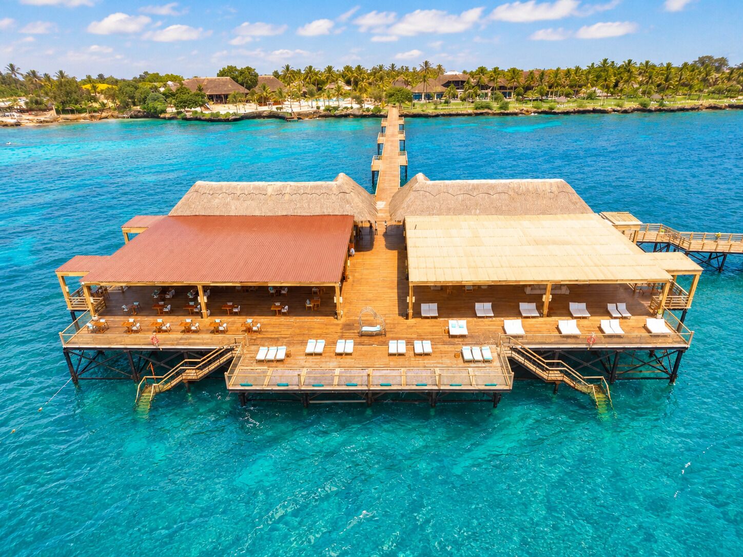 A floating hotel with overwater bungalows, each with a thatched roof and a deck with lounge chairs.