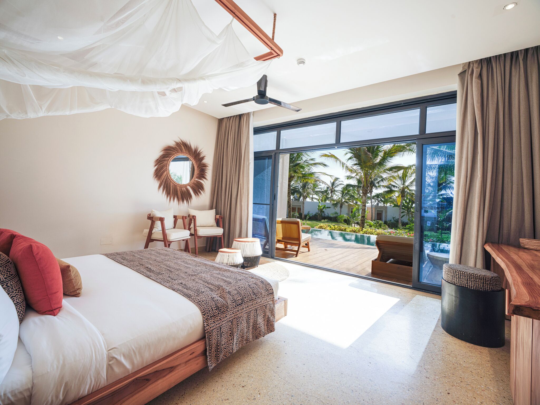 Un dormitorio con una cama grande, ventilador de techo y vista a una piscina y palmeras.