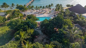 A resort with a pool, palm trees, and a pier extending into the ocean.