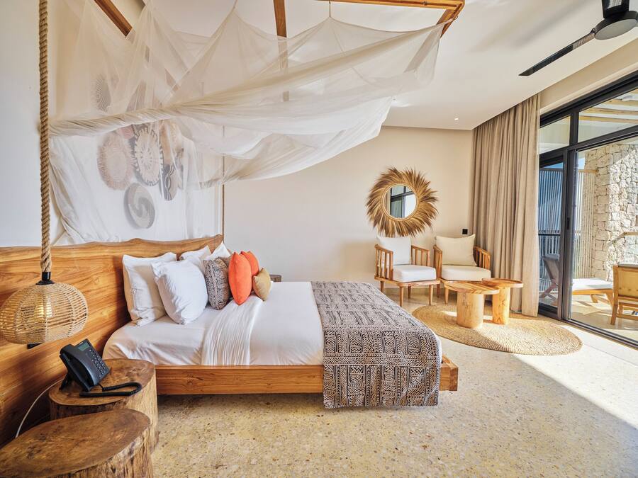A spacious bedroom with a large bed, a wooden headboard, a hanging canopy, and a stone wall.