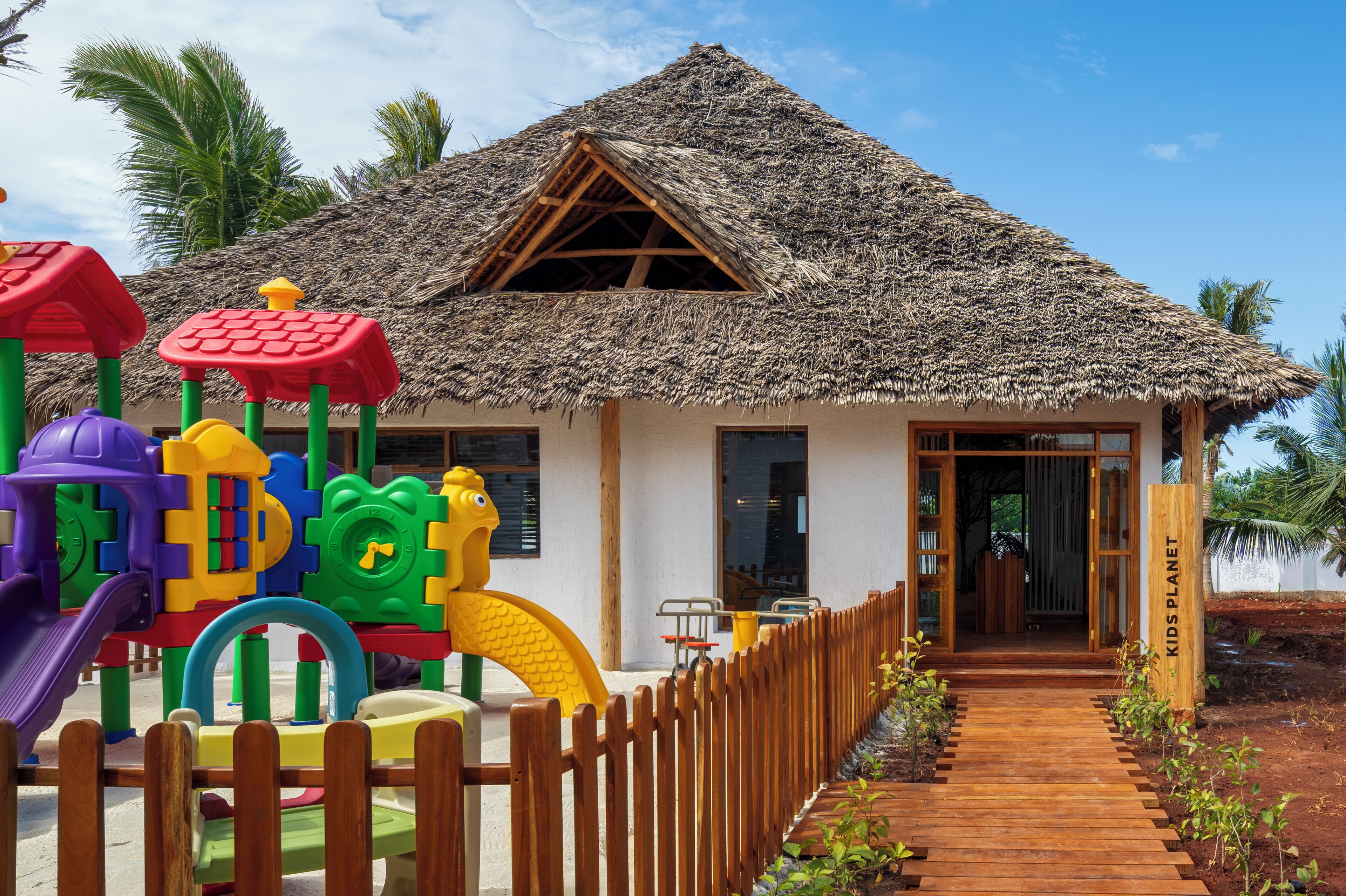 A house with a thatched roof, a wooden fence, and a play area with colorful equipment.