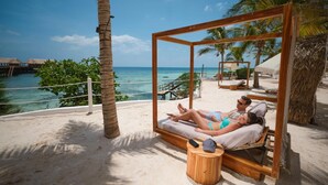 A wooden swing bed with a view of the ocean, a palm tree, and a thatched roof structure.