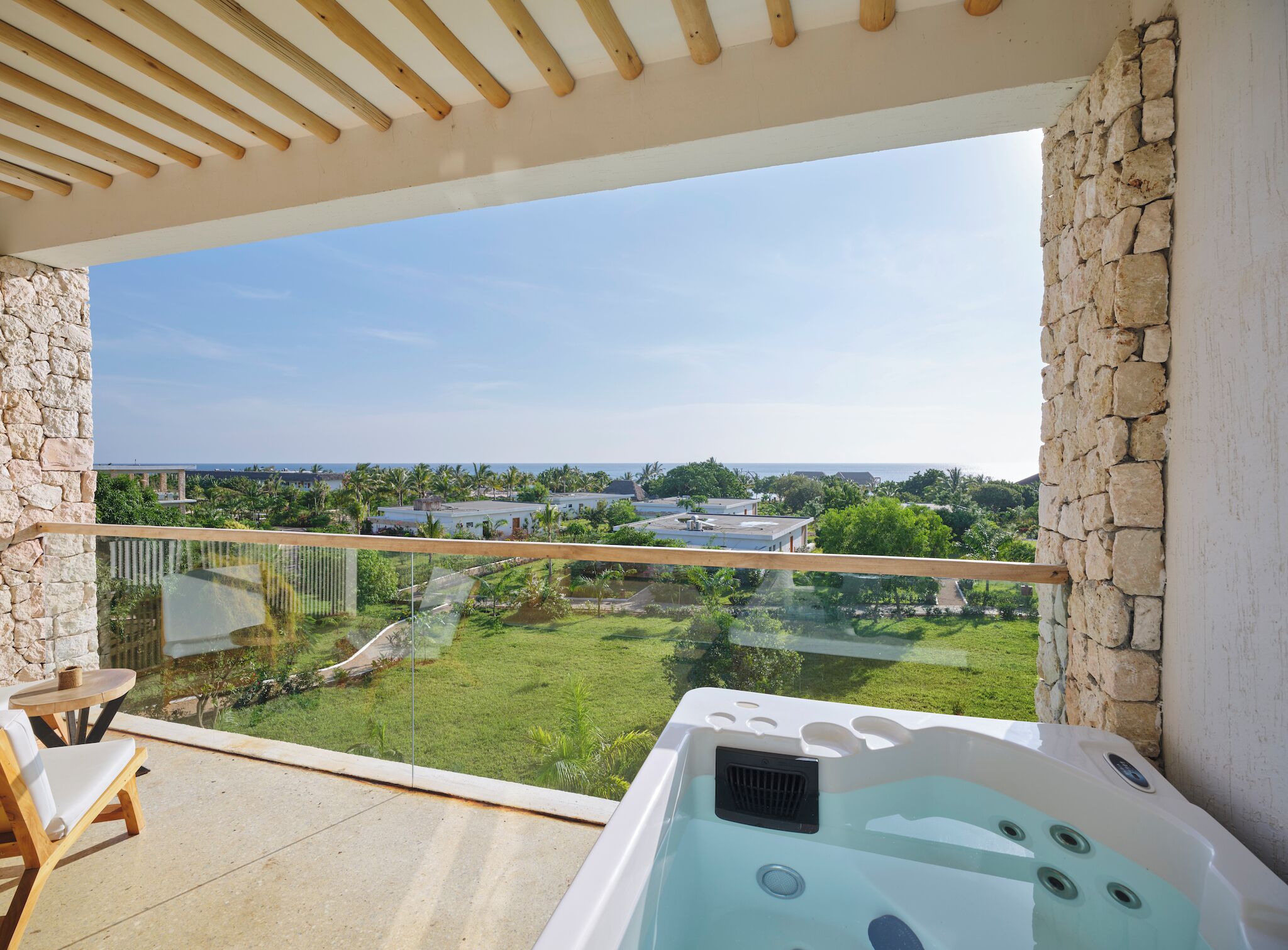 A balcony with a hot tub, stone walls, and a view of a green landscape and buildings.