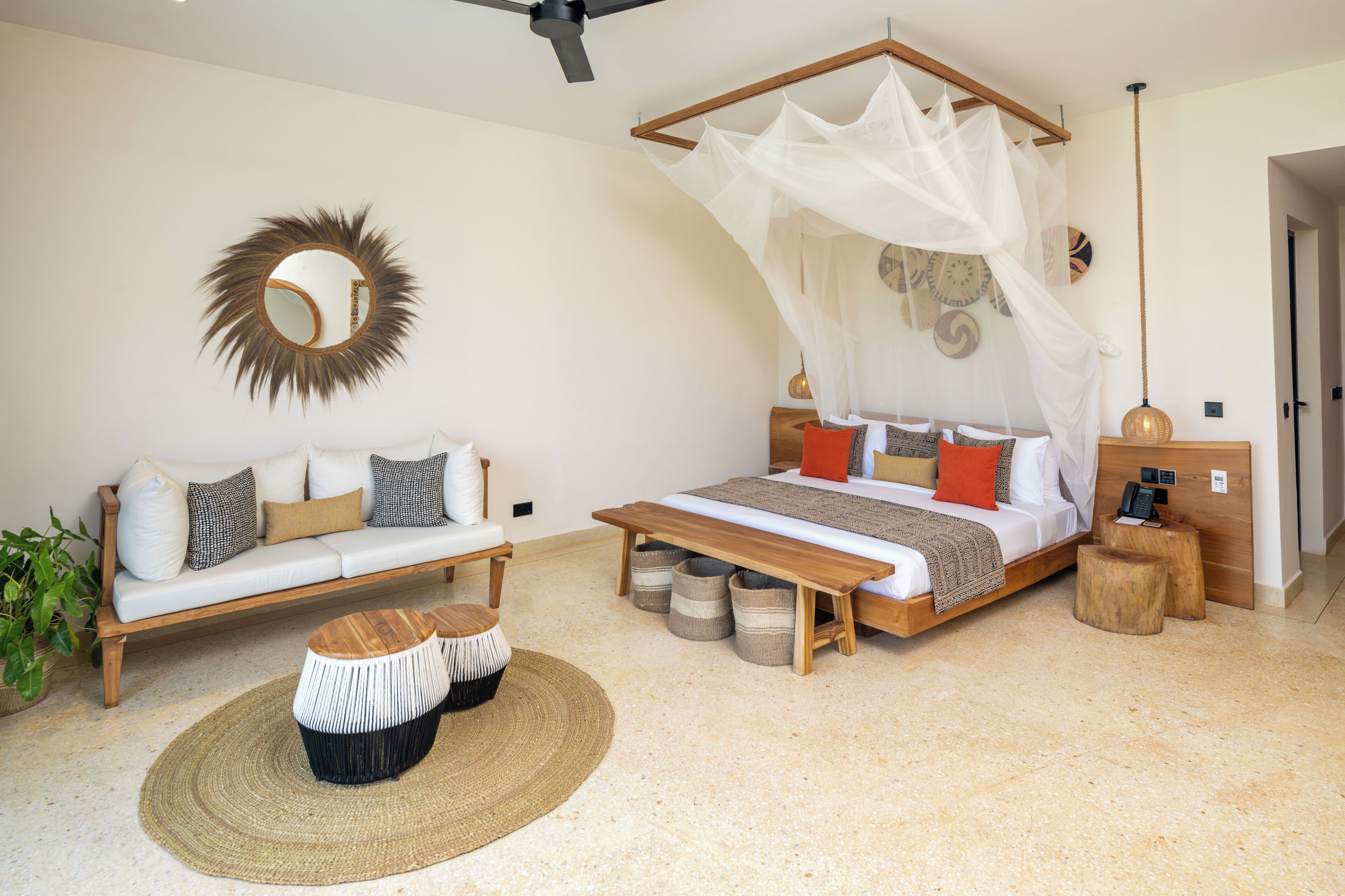 Quarto com cama, sofá, mesa de cabeceira, luminária pendente e espelho.
