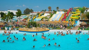 Una piscina grande con varias toboganes y una zona de playa con sombrillas.