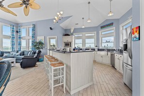 A spacious living area with a large window, a ceiling fan, and a kitchen with white cabinetry and a central island. - Canalfront Dog Friendly Home w/ Hot Tub, Smart TVs, and Private Boat Dock (Frisco)