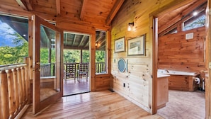A wooden cabin interior with a wooden deck, a bathroom with a sink and toilet, and framed pictures on the wall.