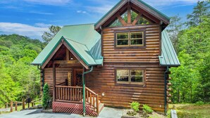 A log cabin with a green roof, a porch, and a staircase leading to the entrance.
