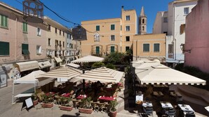 An outdoor café with tables and chairs, surrounded by buildings and a church tower. - Casa dei Liuti (Alghero)