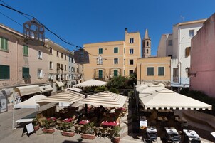 Un café al aire libre con mesas y sillas, rodeado de edificios y una torre de iglesia.