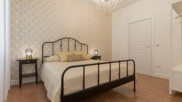 A bedroom with a bed, two bedside tables, a chandelier, and a door.