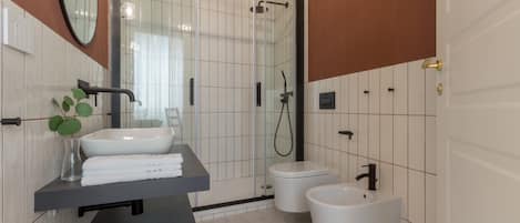 A modern bathroom with a glass-enclosed shower, a pedestal sink, and a bidet.