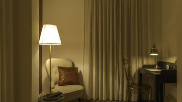 A hotel room with a bed, a chair, a desk, a lamp, and a clock.