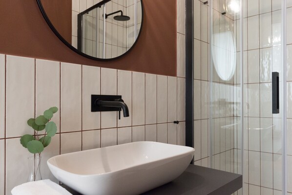 Un baño moderno con un lavamanos grande tipo cuenca, un espejo redondo y una cabina de ducha de vidrio.