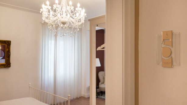 A hotel room with a chandelier, a bed, a door with a number plaque, and a framed picture on the wall. - Casa dei Liuti (Alghero)