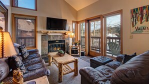 A cozy living room with a fireplace, leather sofas, a wooden coffee table, and a television mounted above the fireplace. - Walk across the street to the Snowflake Chair! Beautiful 4BR Condo with great am (Breckenridge)