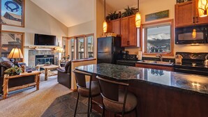 A modern kitchen with a large island, wooden cabinets, and a view of mountains through the window. - Walk across the street to the Snowflake Chair! Beautiful 4BR Condo with great am (Breckenridge)