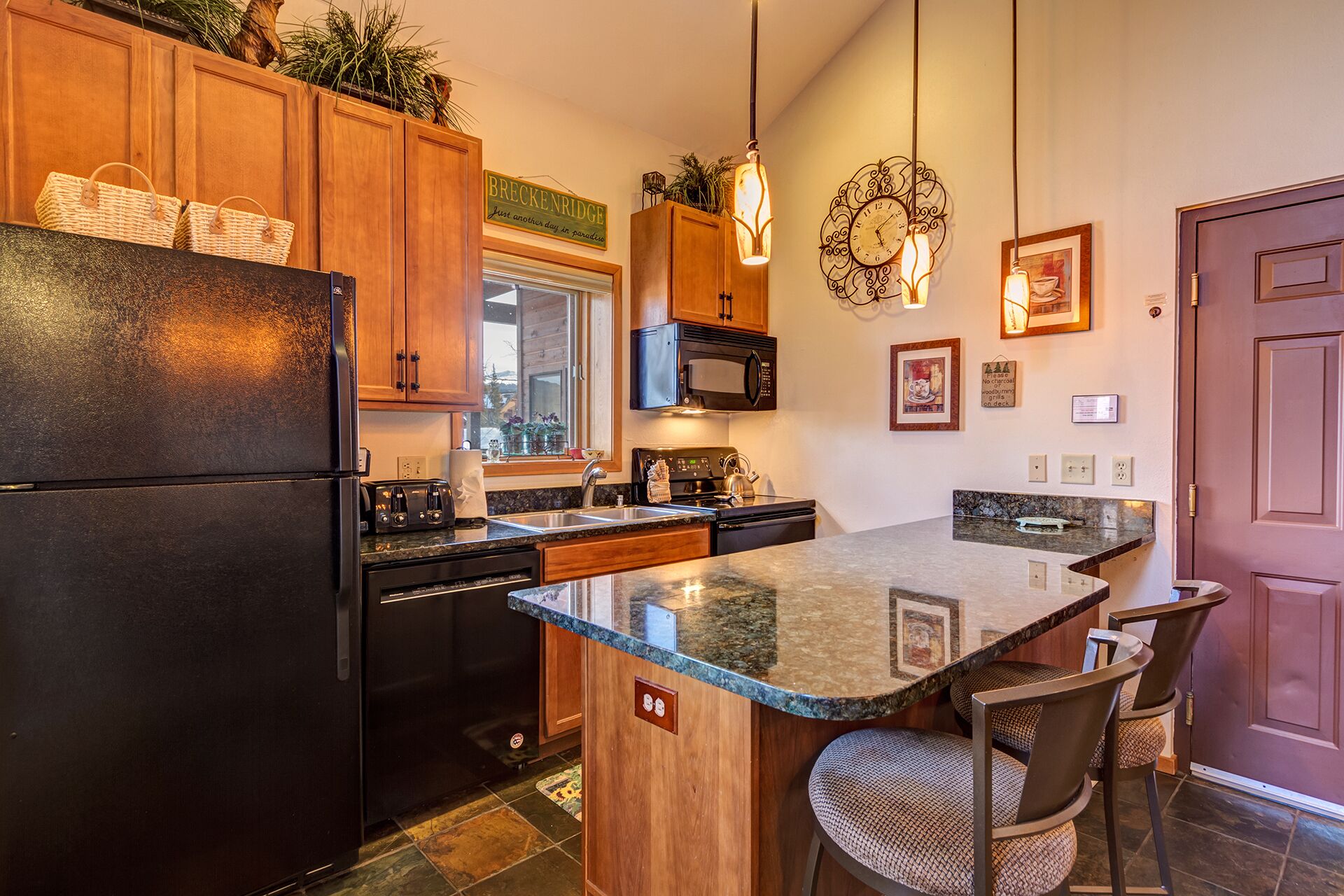 A modern kitchen with wooden cabinets, a black refrigerator, a microwave, and a granite countertop.