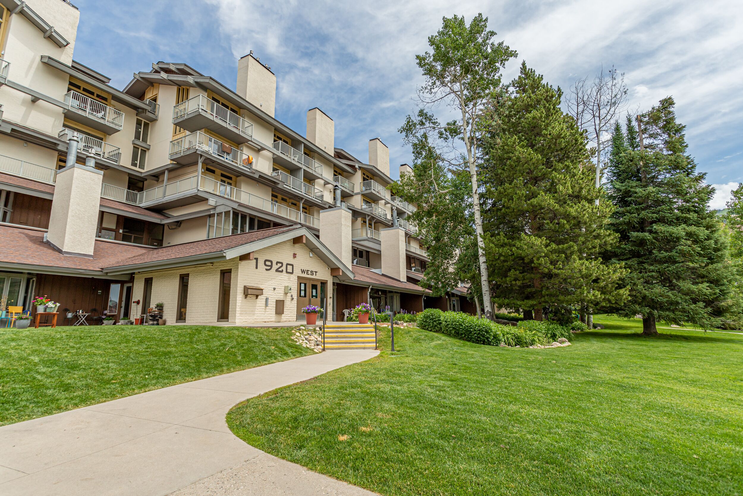 A multi-story residential building with a flat roof, balconies, and a well-maintained lawn.
