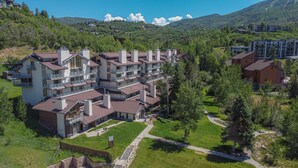 Ein mehrstöckiges Hotel mit Balkonen, umgeben von Grün und einer Bergkulisse.